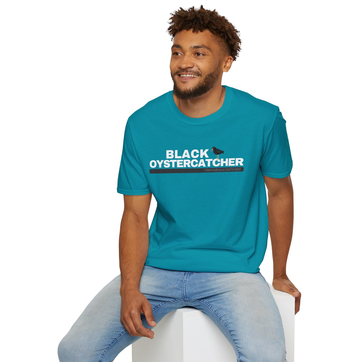 Man wearing a blue t-shirt with 'Black Oystercatcher' text sitting on a white stool against a white background