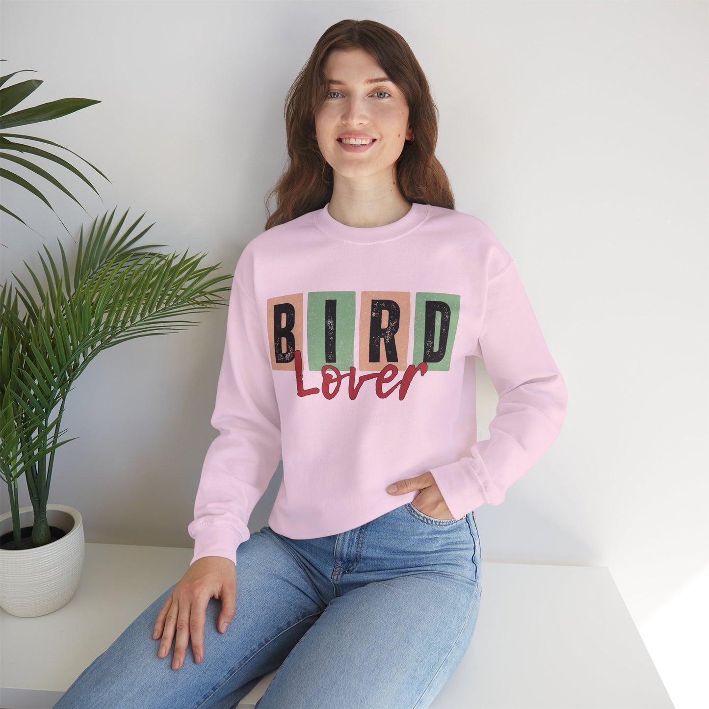Person wearing a pink sweatshirt with 'Bird Lover' text, sitting in a room with a plant.