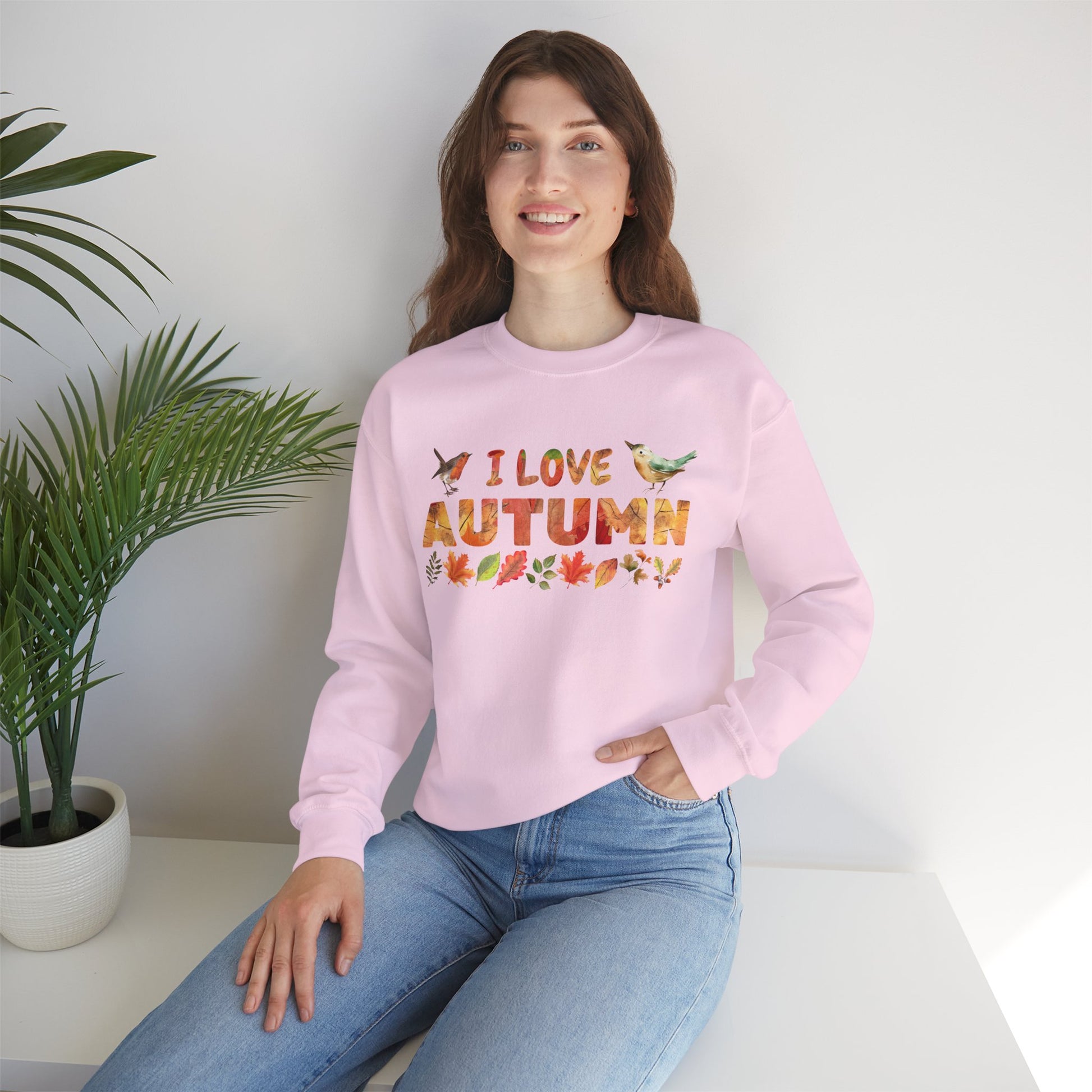 Woman wearing a pink sweatshirt with 'I love autumn' text, sitting in a room with a plant.