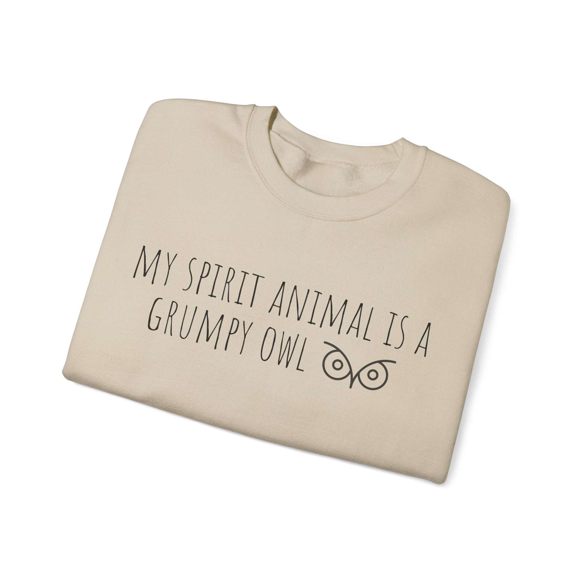 Folded beige sweatshirt with text 'My spirit animal is a grumpy owl' on a white background