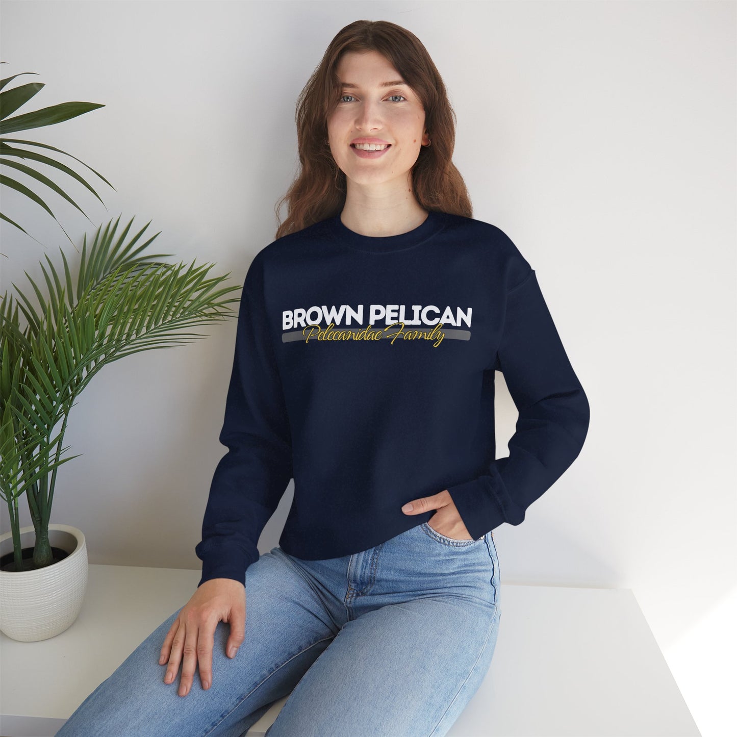 Person wearing a navy blue sweatshirt with 'Brown Pelican' text, sitting on a white surface with a plant in the background.