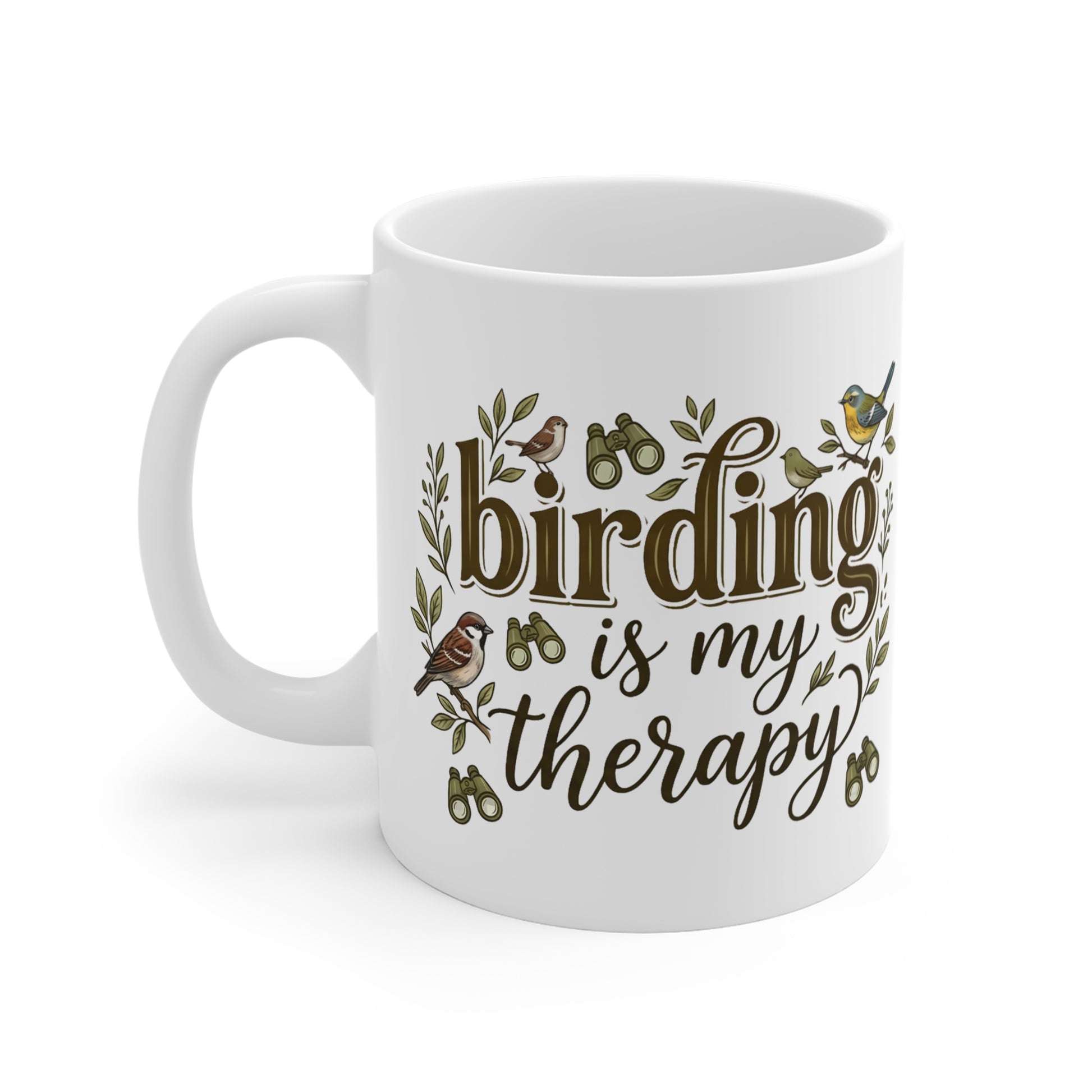 A white ceramic mug with a handle, featuring the printed phrase 'birding is my therapy' in brown script and serif fonts, decorated with small bird illustrations and green leaves on a white background.
