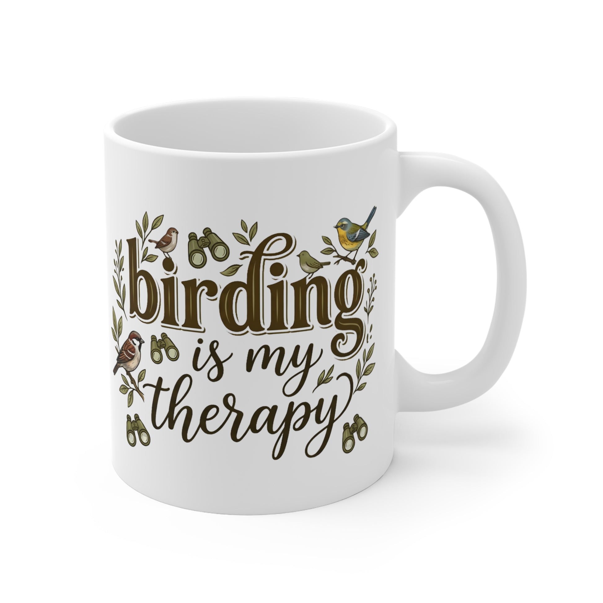 A white ceramic coffee mug with a handle, featuring the phrase 'birding is my therapy' in brown script and serif fonts, decorated with small bird illustrations and green leaves.