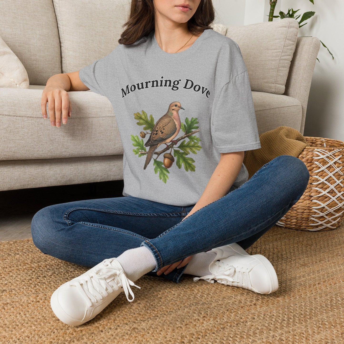 Person wearing a sports gray t-shirt, text Morning Dove, with a dove graphic design sitting on a couch.