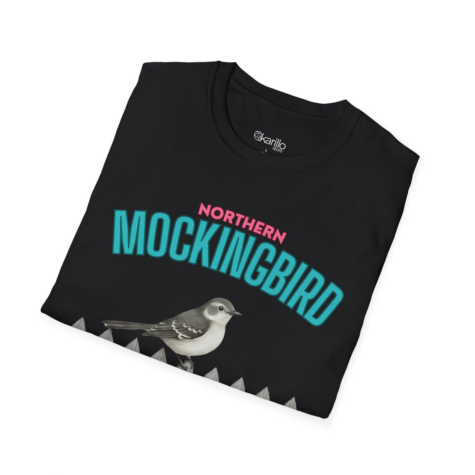 A folded black t-shirt with a graphic print featuring the text 'NORTHERN MOCKINGBIRD' in teal and pink, an illustration of a mockingbird perched on a white picket fence with green foliage, with white background.